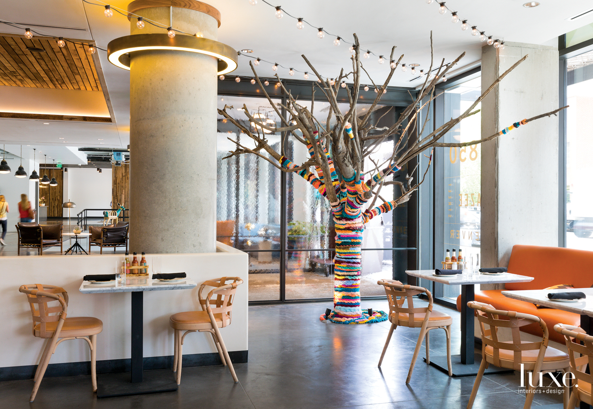 interior of a cafe with a large tree wrapped in multicolored yarn strings artwork