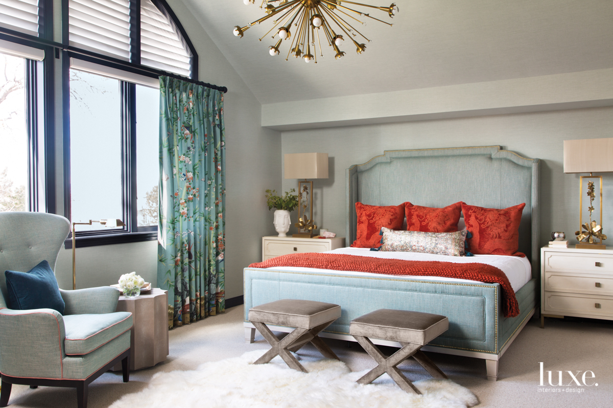 In the master suite, a Phillip Jeffries wallcovering provides a soothing backdrop for a bed upholstered in a Castel fabric. Tomato-red throw pillows by Ivystone are a bright accent. John Richard's Blooming Pierced Orchid table lamps sit on Vanguard nightstands. The stools and light fixture are all by Jonathan Adler.