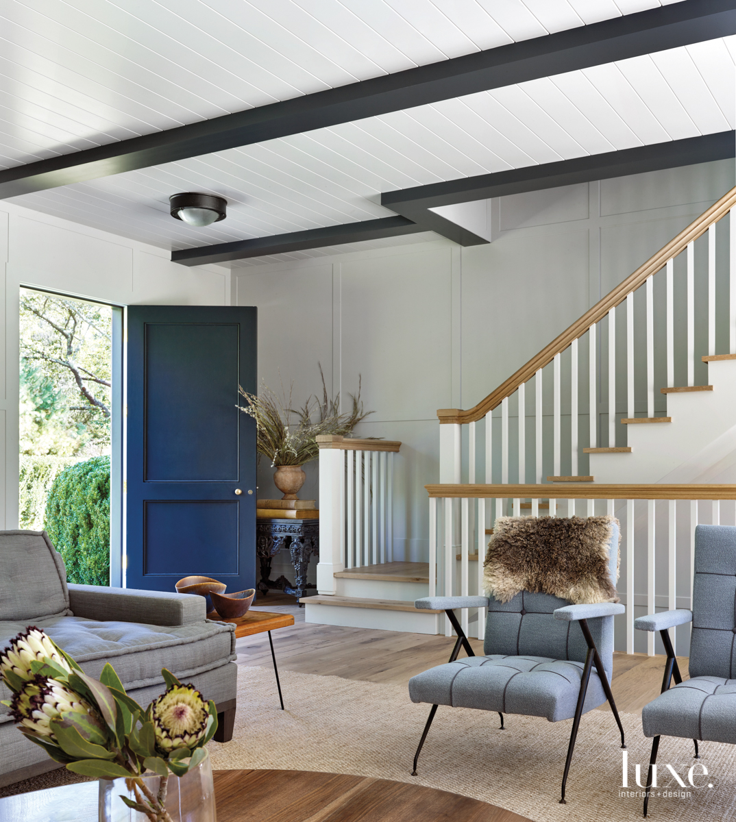 In a couple's farmhouse-style vacation retreat in East Hampton, the front door opens onto the living room, where an Ico Parisi lounge chair from RE Steele, one of a pair, is upholstered in bouclÃ© wool fabric and accented with a fur throw. &quot;Although the color palette and textures were inspired by the beach, we wanted the home to feel comfortable year round,&quot; says designer Dan Scotti.