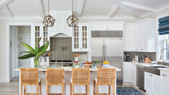 Serena & Lily's Balboa counter stools are tucked under the kitchen island's Calacatta marble countertop. Vaughan's Fenton lanterns hang above, and Wolf appliances outfit the space.