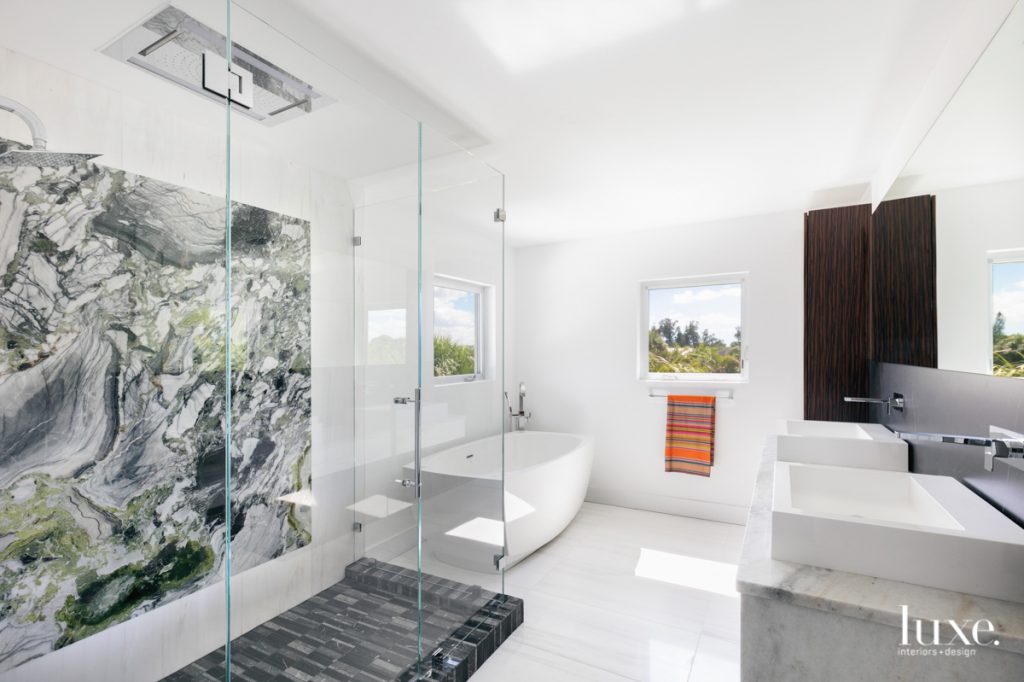 The master bathroom is a serene refuge. A vivid slab of green-streaked marble purchased at Eagle Stones Corporation makes a statement in the shower, along with Aquabrass fixtures and textured Nero Marquina marble tiles. The BainUltra tub sits on white marble from Oracle Flooring and Design.