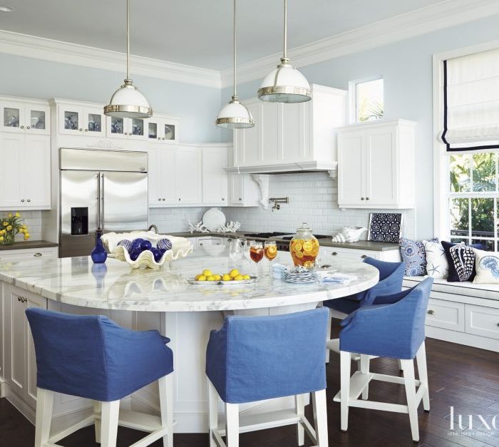 In the kitchen, Lee Industries stools surround the Carrara marble island top, refinished by Mario Ferazzoli & Son. Samuel & Sons tape outlines the Roman shades in Duralee fabric. Wellborn Cabinet’s cabinetry from DeStefano Designs and Restoration Hardware pendants already existed in the home.