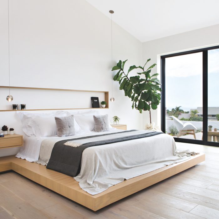 minimalist bedroom with white bed on wood platform and natural light