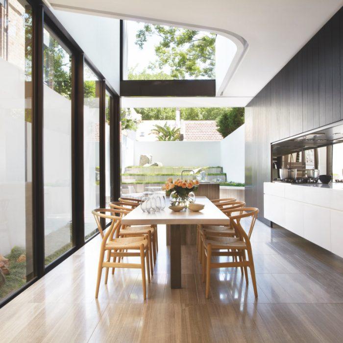 Sydney's Smart Design Studio created this open-air kitchen as part of a modern addition to a Federal-style house. Walls of windows and retractable glass doors bring in an abundance of light, which a mirrored backsplash further reflects. As a result, the narrow space feels much larger than it is.