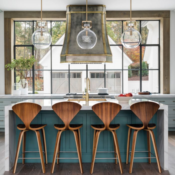 In the kitchen, a trio of spherical pendants hangs above a Bianco Lasa Fantastico marble-topped island fabricated by Construction Resources. The base is painted Sherwin-Williams' Riverway, while the reproduction Norman Cherner walnut counter stools are from Design Within Reach. The vent hood is by Francois &amp; Co.