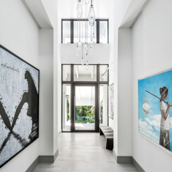 The Florida Waterfront Home Primed For Art Lovers And Outdoor Entertaining A glass WSI pivot door opens to the foyer of a renovated Coral Gables home by designer Carolyn McCarthy. The drama continues with Hammerton Studio’s Aalto pendants as well as La Isla Aquella by Jose Bedia (left) and Dreamcatcher by Sandro de la Rosa (right). Artefacto’s Sweep bench rests on leathered marble flooring from Innovative Surfaces.