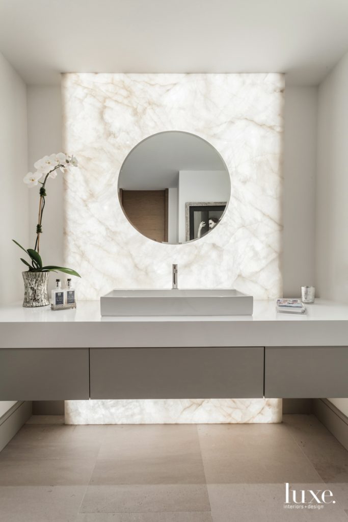 In the powder room, Krome Construction suspended the cabinetry--consisting of a quartz countertop from Innovative Surfaces and a Florense vanity base from Armazem--in front of a backlit wall of Opustone's Lumix quartzite. A beveled mirror by CM Glass hangs above Hastings' Quad ceramic sink and Franz Viegener's Lollipop faucet from Coral Gables Kitchen & Bath.