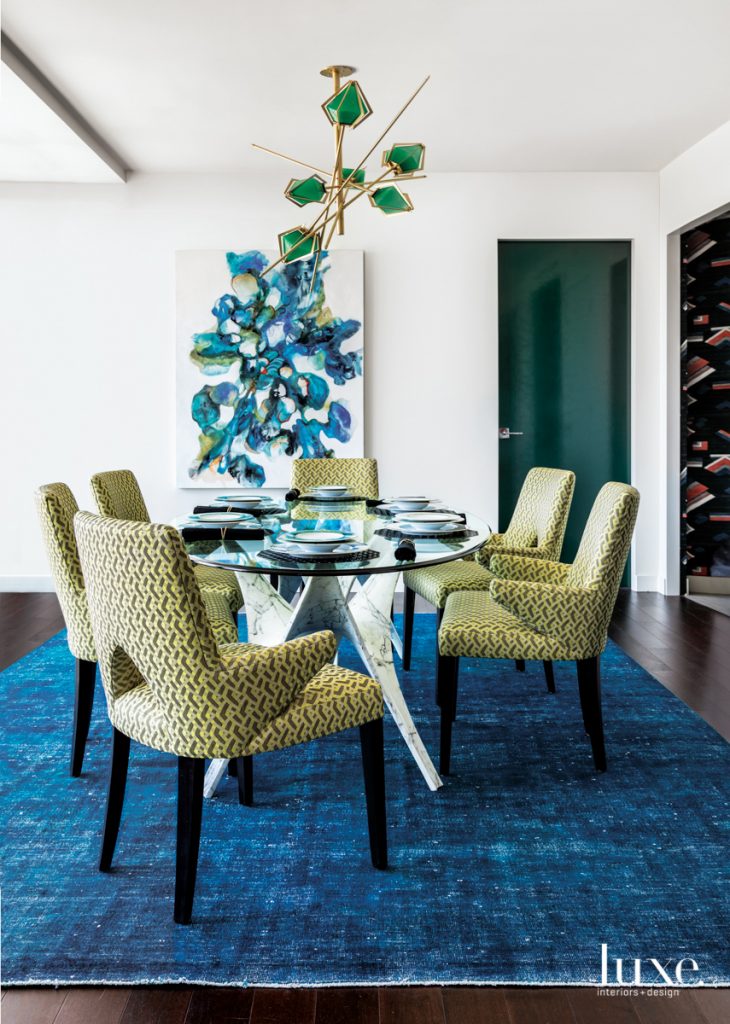 Blues and greens saturate the dining room via the Gabriel Scott chandelier, a vintage cobalt-blue over-dyed kilim rug from Kilim Studio and art by Cookie Ashton. The Ambella Home Collection dining table pairs with chairs upholstered in a Rubelli textile from Donghia.