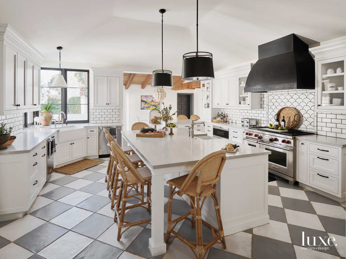 The kitchen is home to a checkered floor, wooden barstools and design details, black light fixtures and white cabinets, backsplash and countertops
