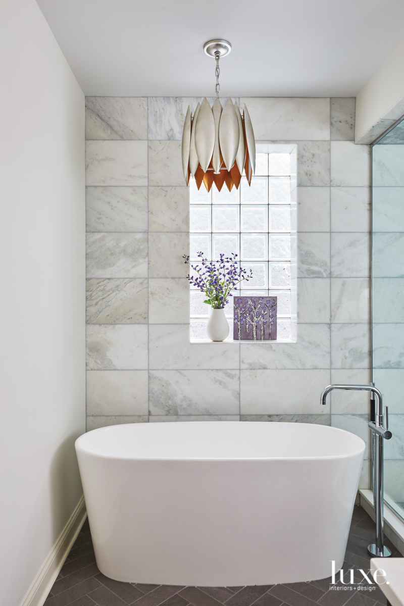 bathrub with light fixture agove and marble wall behind the tub