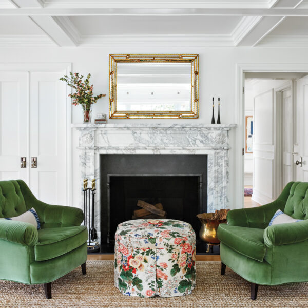 A Little Bit Of The Unexpected Makes A Designer’s Chicago-Area Home Sing A seating area in front of the living room fireplace with green velvet chairs, a floral ottoman and a vintage mirror.