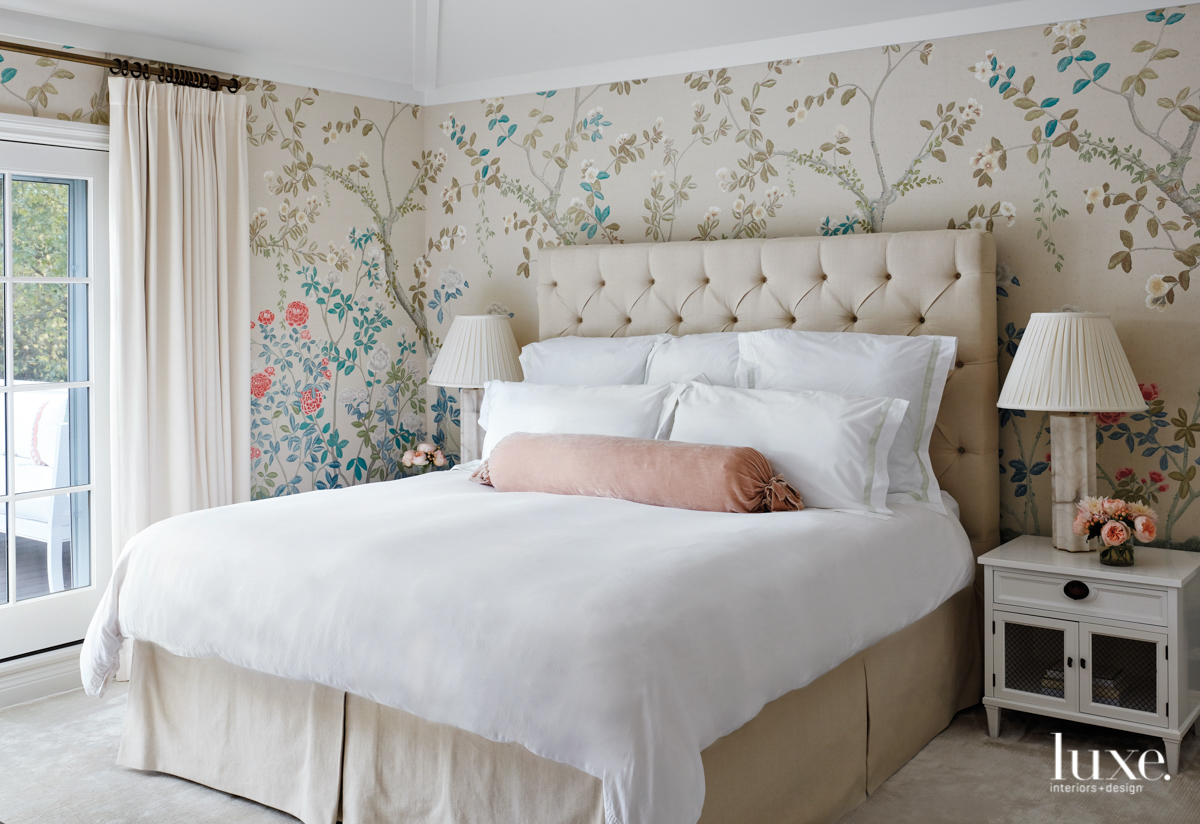 The master bedroom has a floral wallcovering and neutral upholstered bed.