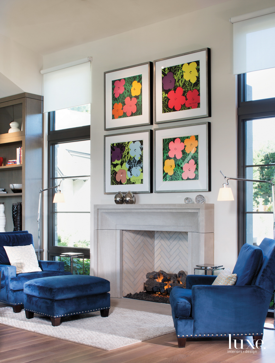 A seating area by the fireplace features plush blue chairs and four brightly colored Andy Warhol prints.