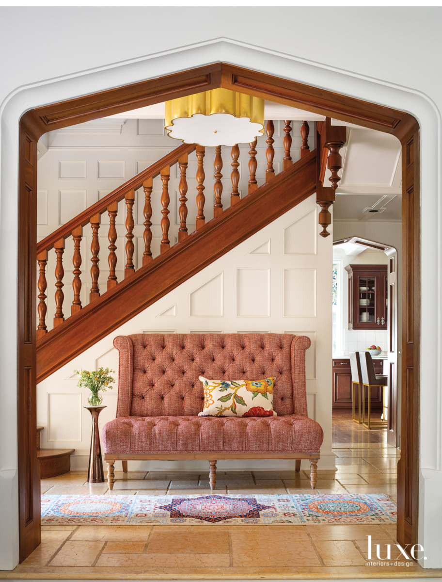 The original stair rail shines in the new white interior. Beneath it is a rose-colored settee.