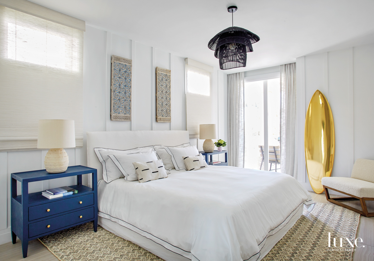 guest bedroom with a black chandelier, blue side tables and a gold surfboard