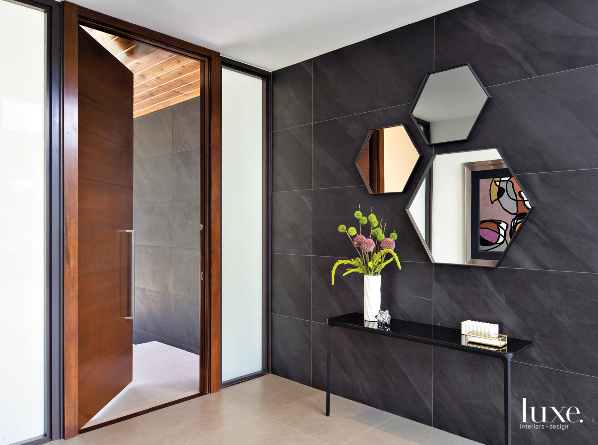 modern foyer with black porcelain tile wall, mahogany front door and geometric mirrors