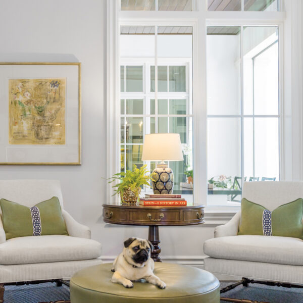 Why Choose Just One? This Florida Home Mixes Tropical Style With Southern Charm sitting area with tall windows, white arm chairs, green table with a dog