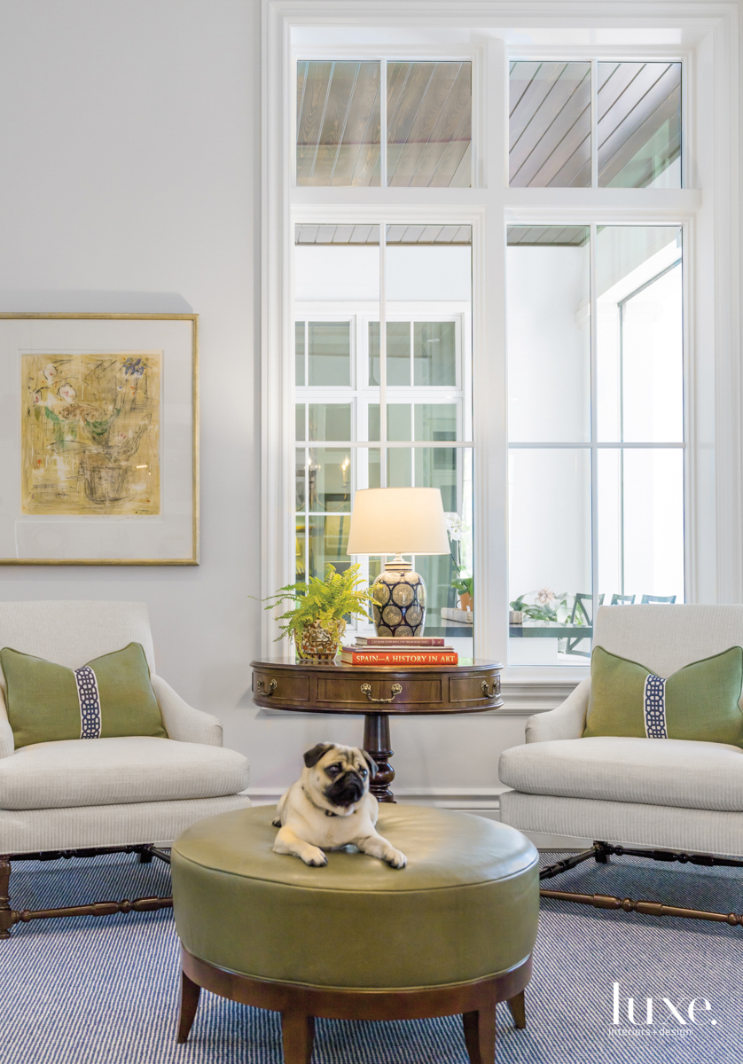 sitting area with tall windows, white arm chairs, green table with a dog