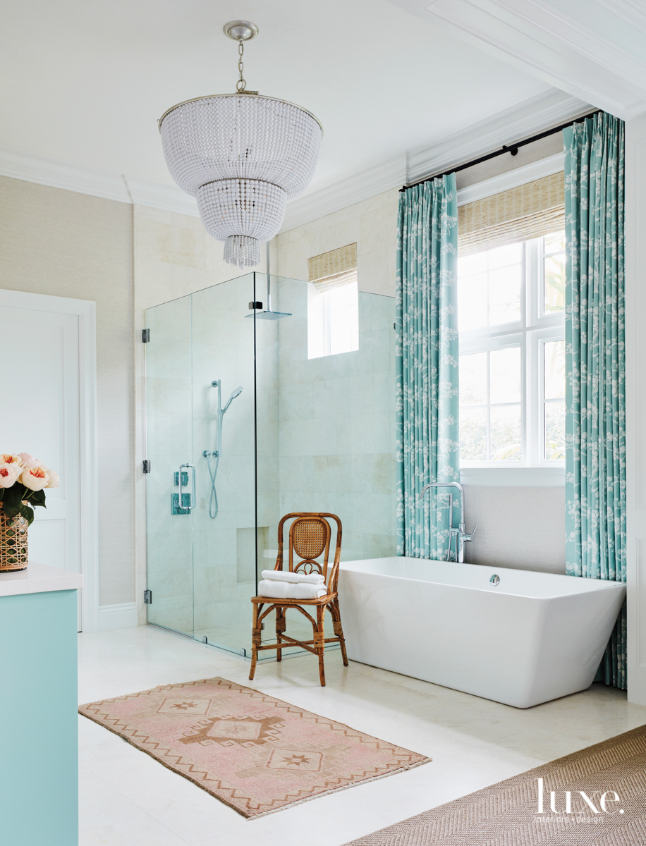 Master bathroom with chandelier, white tub and aqua draperies