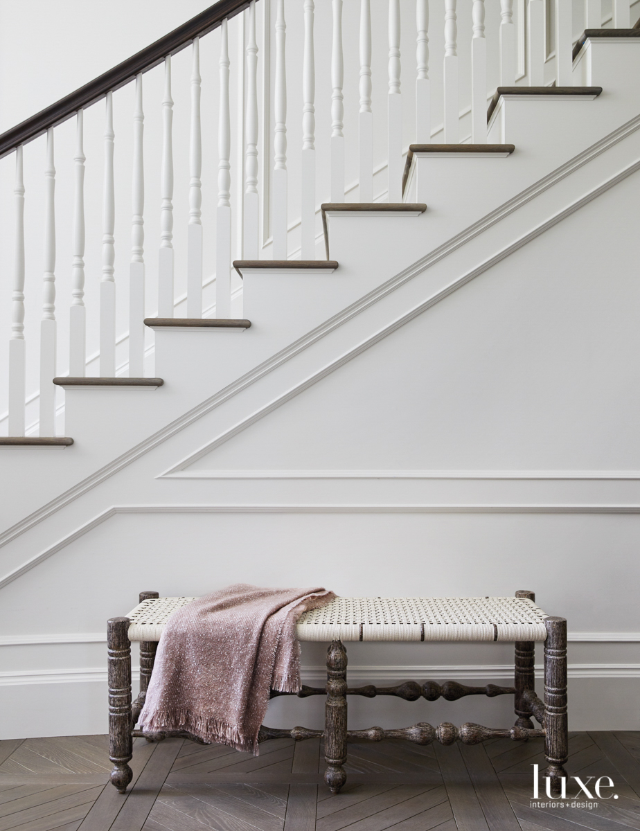 A bench with a woven seat sits alongside a staircase with Victorian details.