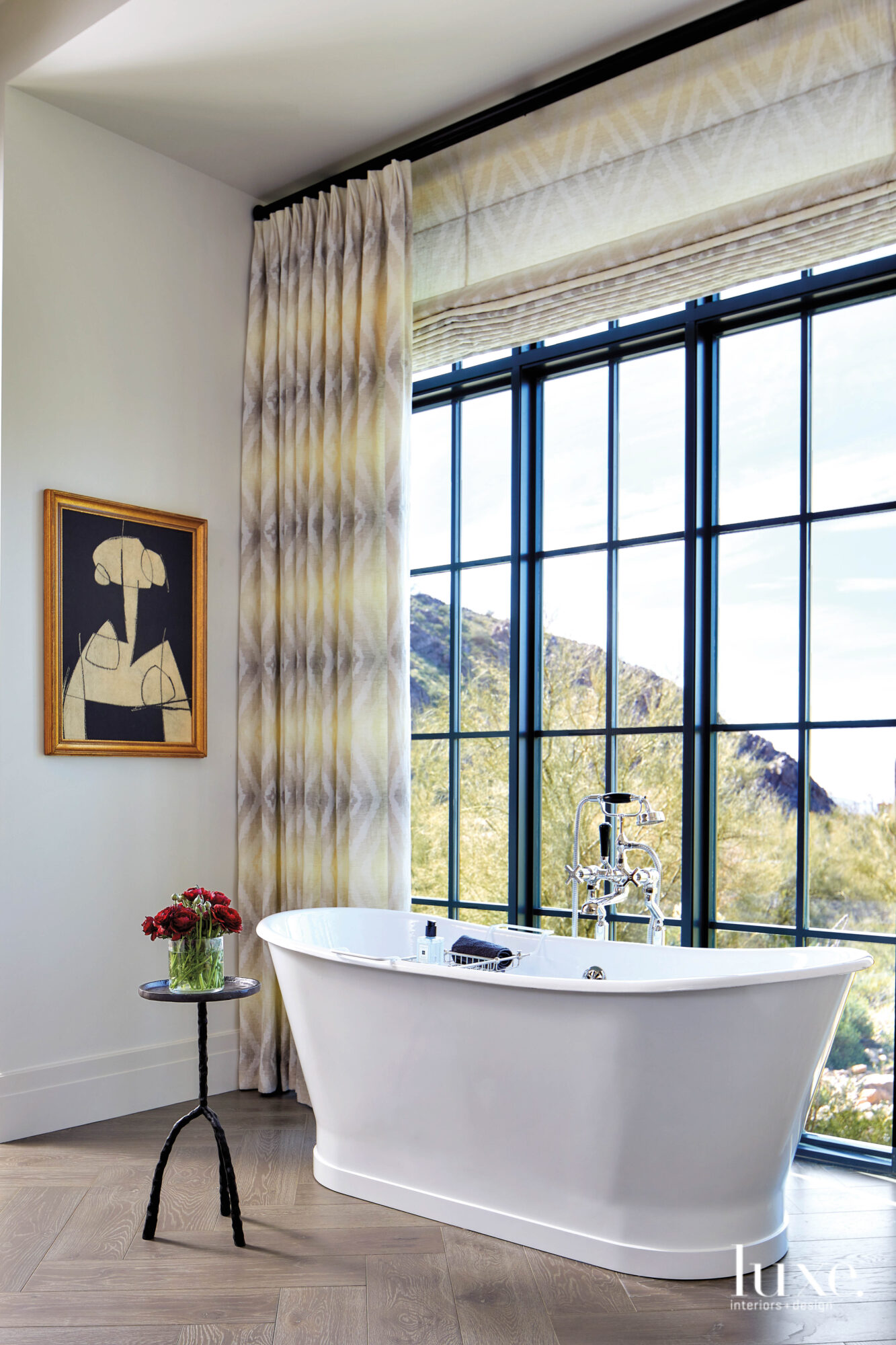 A freestanding bathtub sits in front of a large window in the master bathroom