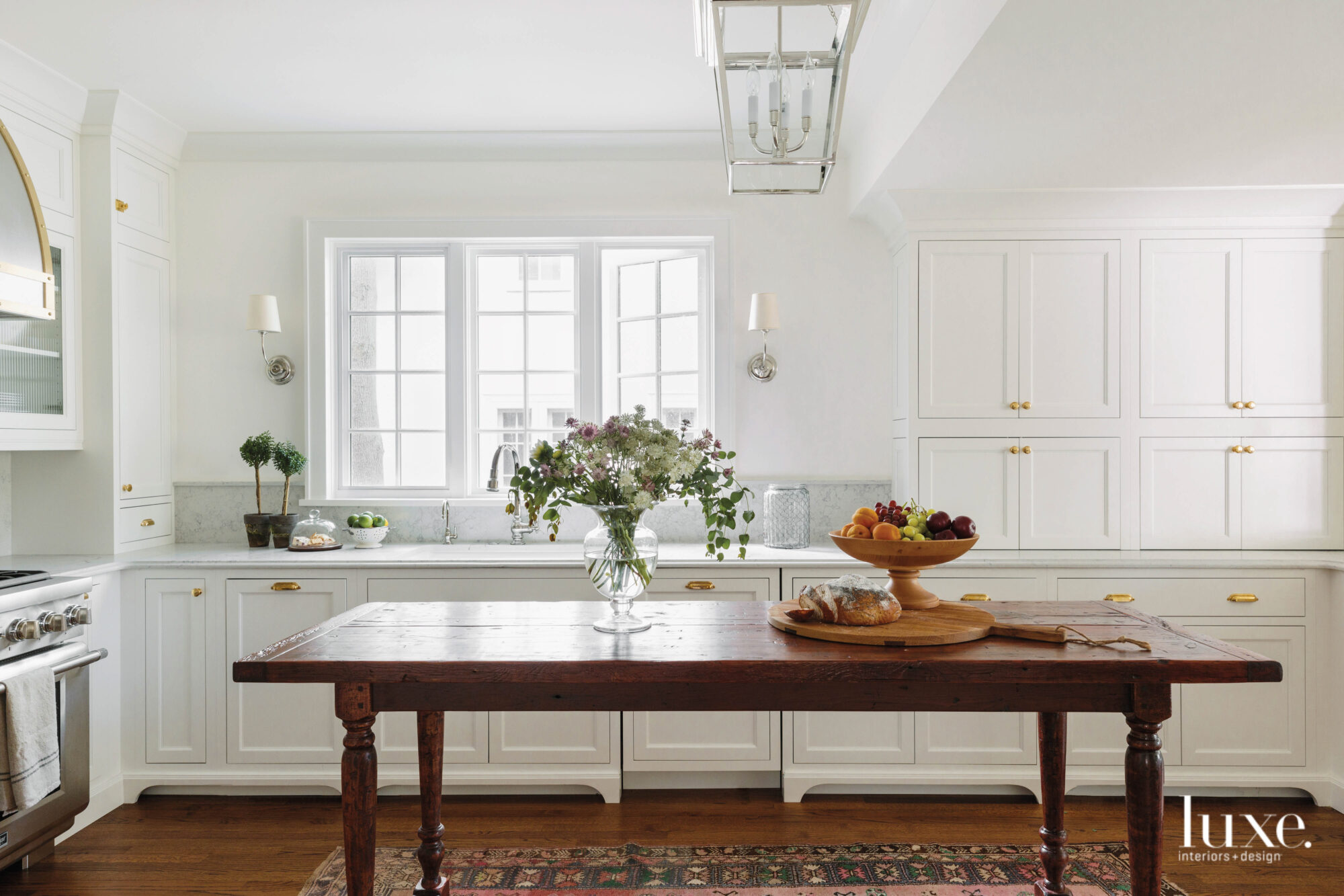A wooden island table takes center stage in the bright, all-white kitchen