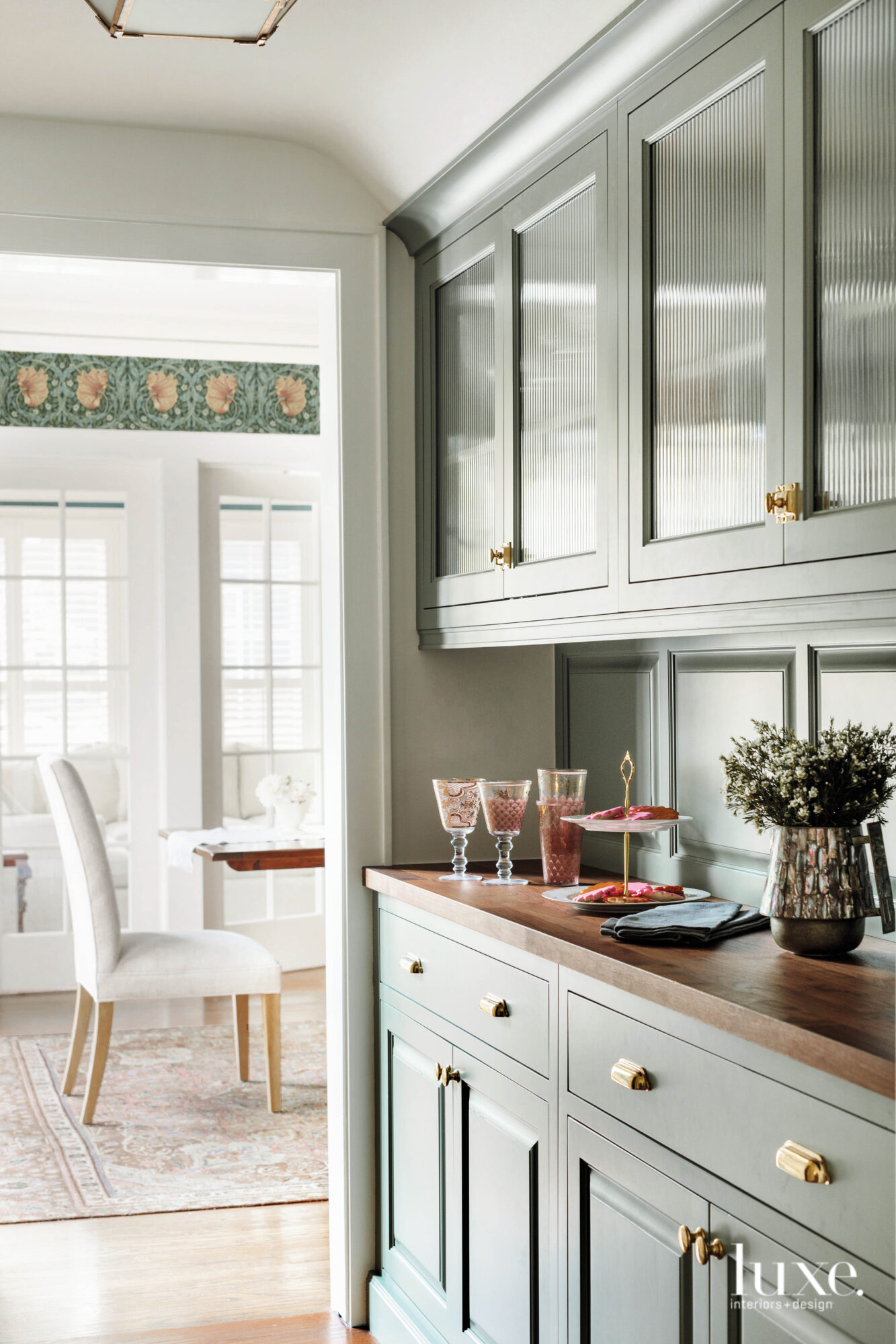 Moss-colored cabinetry in the pantry compliment the wallpaper of the adjacent dining room