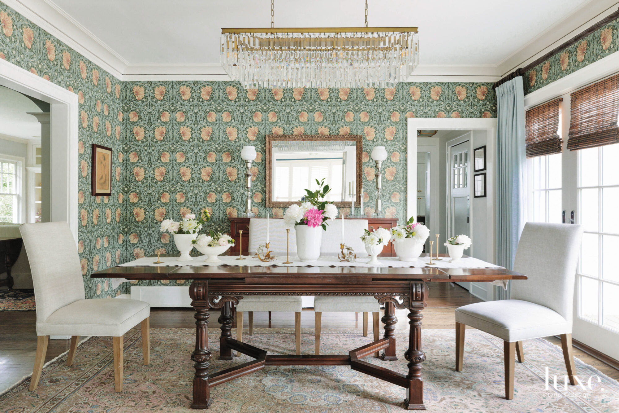 A grand wooden table topped with white flowers is centered in the dining room, surrounded by an eclectic, moss green wallpaper