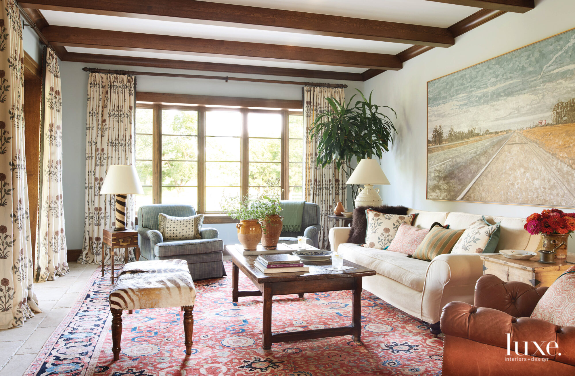A living room has a vibrantly colored rug (mostly red) and vintage and new furniture pieces.