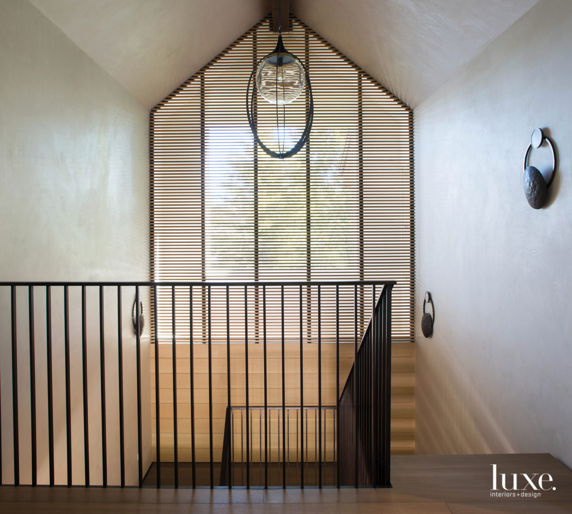 A stairway features a slatted window and a statement light fixture.