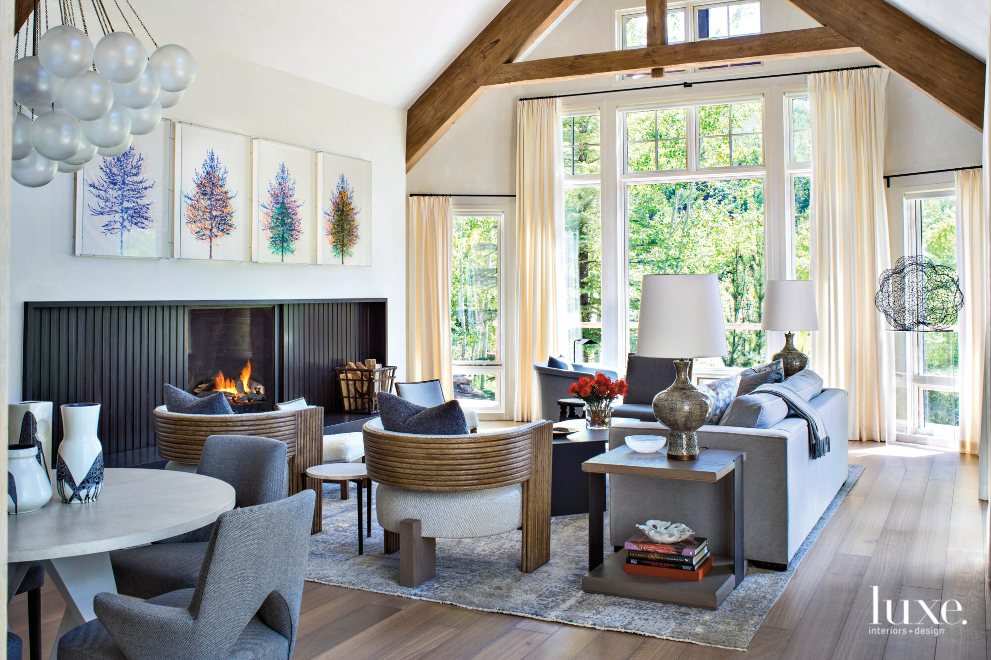A living room is arranged around a fireplace. A row of colorful tree artwork hangs above the mantle.