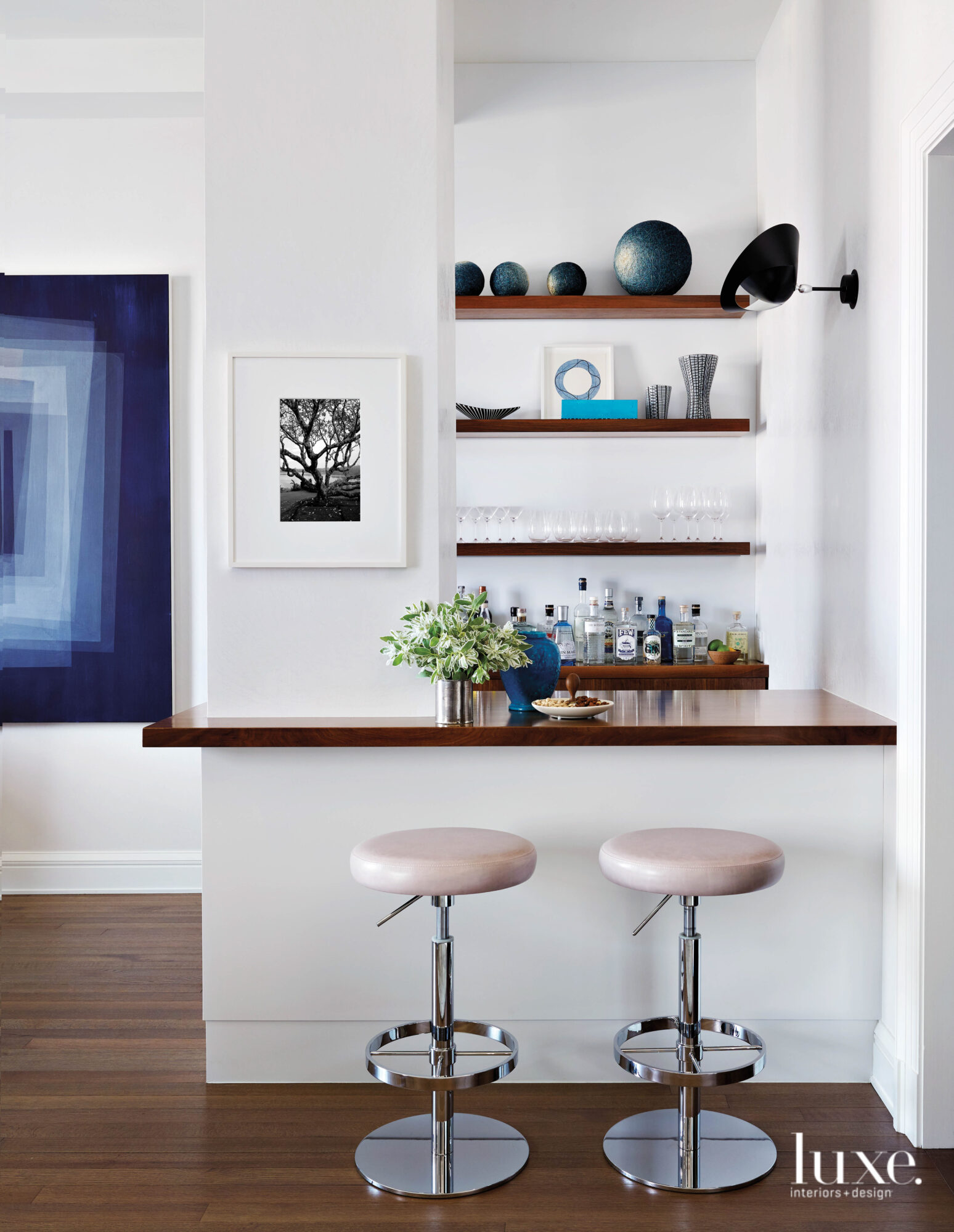 A simple dry bar sits in a corner of the living room, clad with shiny wood counter tops and shelves.