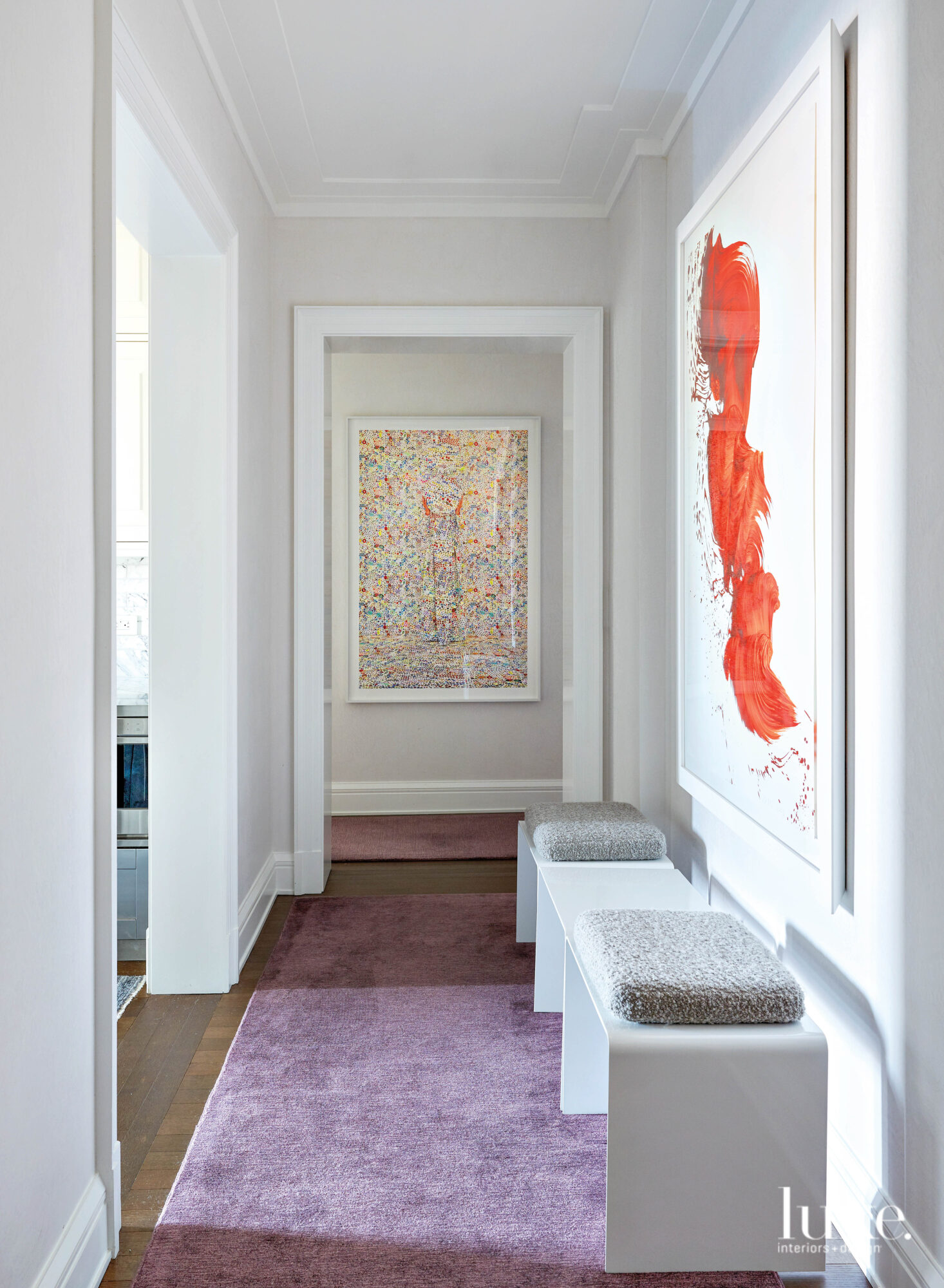 A wide hallway with benches sitting in front of a bright accent painting.