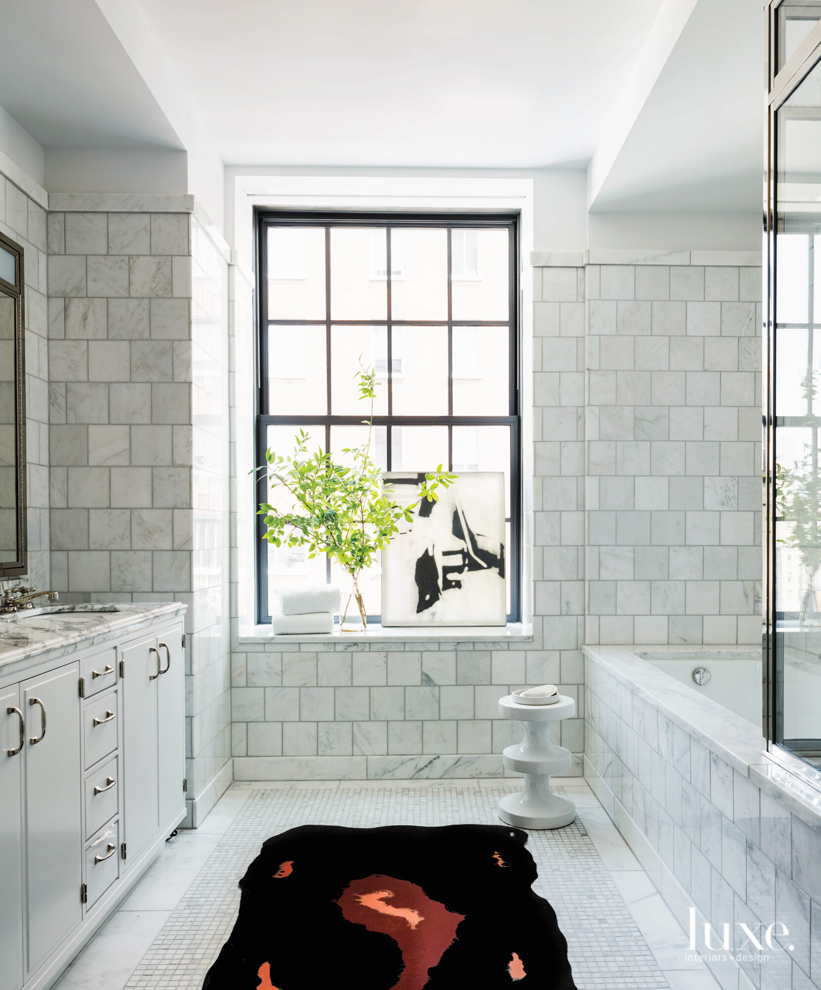 A bright window floods the master bath, clad with marbled tiles and brass finishes, with light
