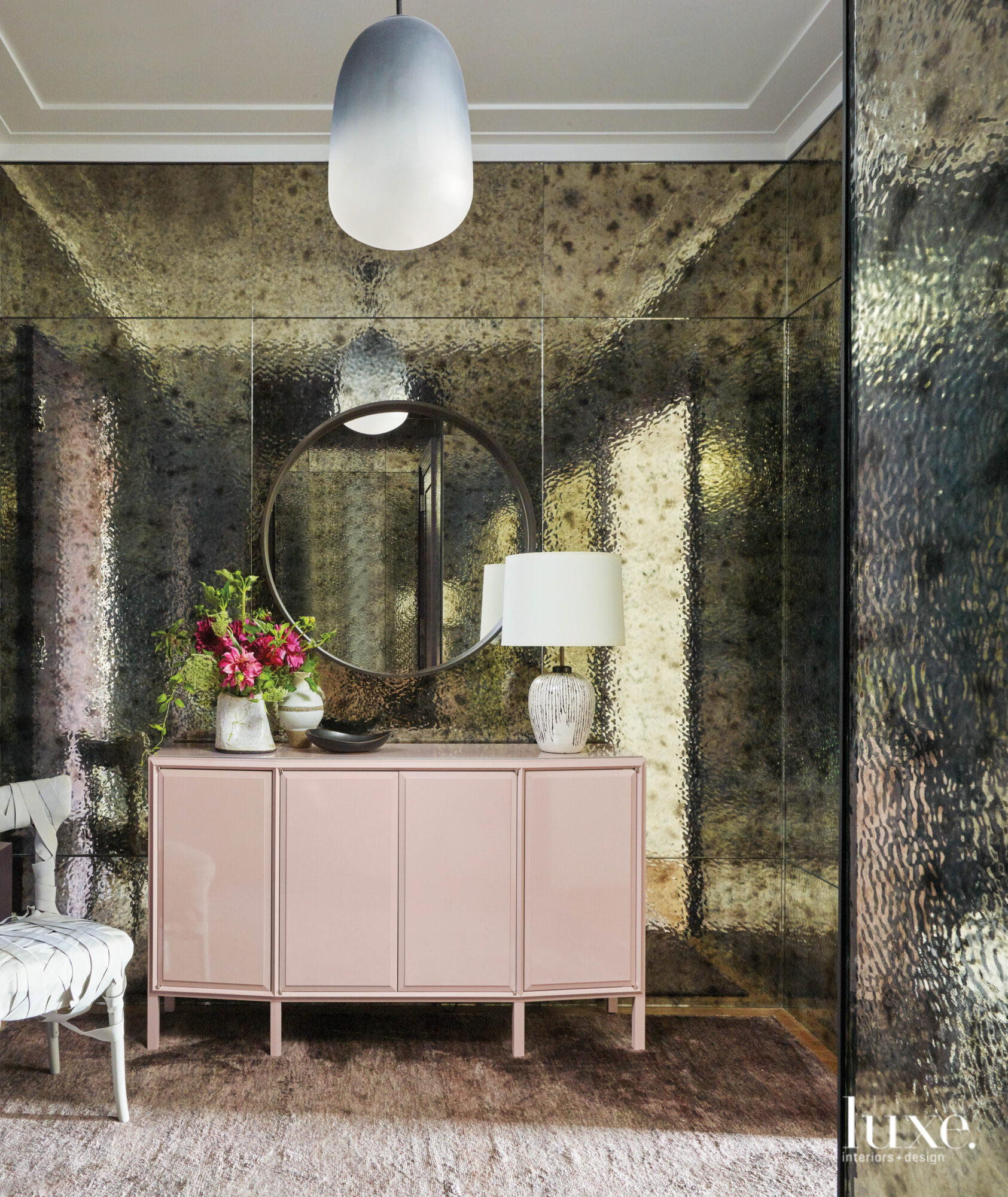 An antique, reflecting wall welcomes all who enter the apartment; a pink cabinet sits facing the door.