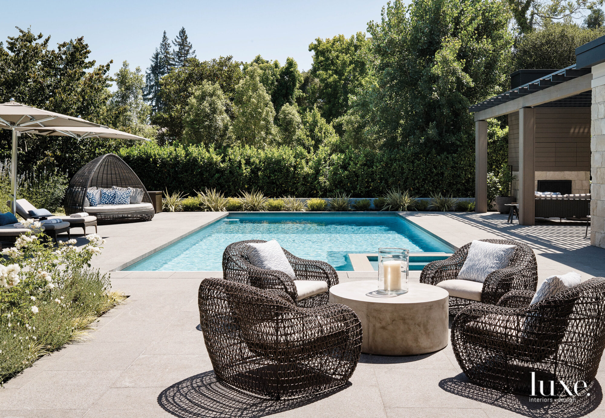 A pool has an entertaining area beside it outfitted with a circle of four lounge chairs.
