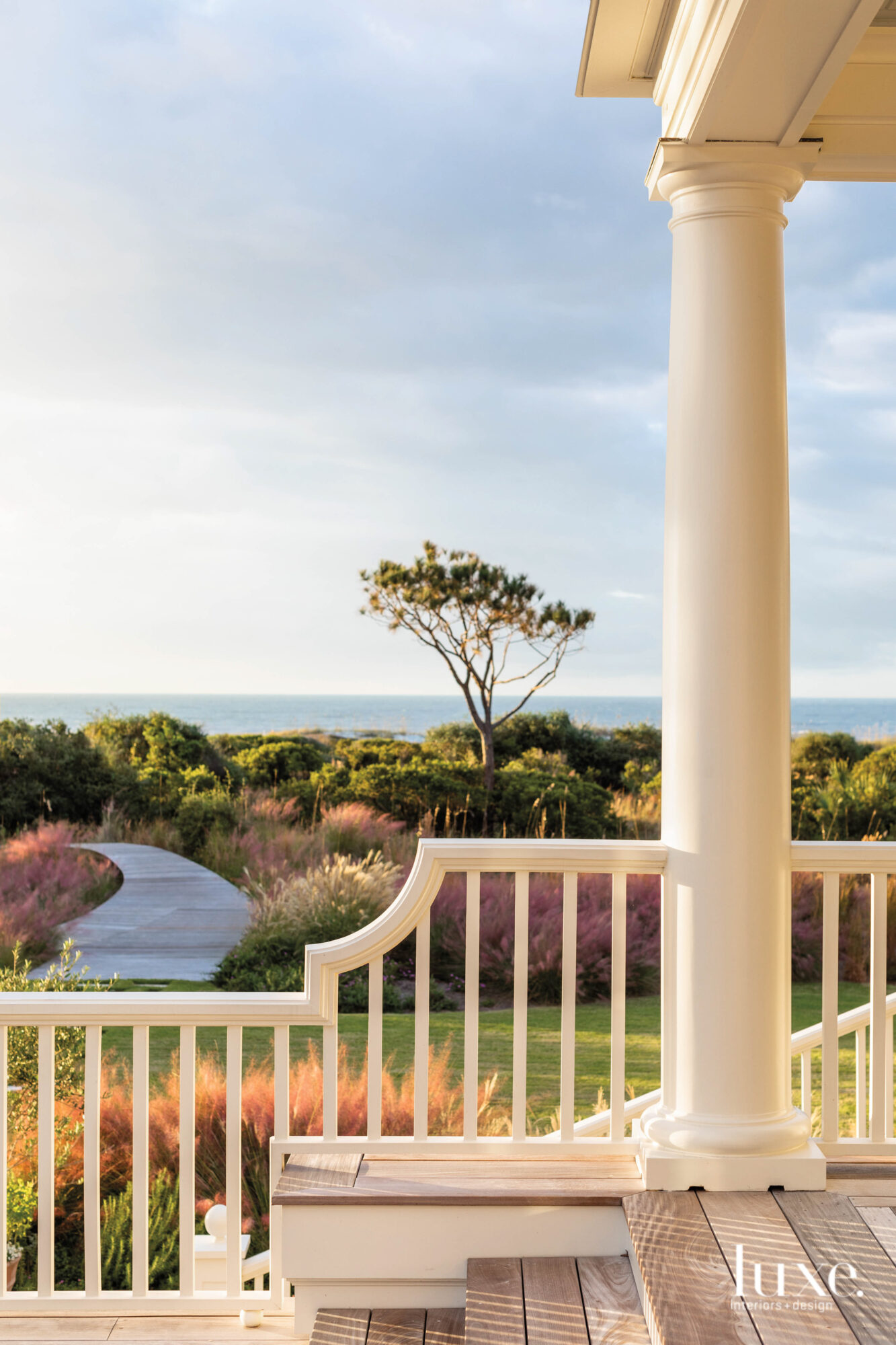 Porch railing and column with view of ocean, boardwalk and native plants