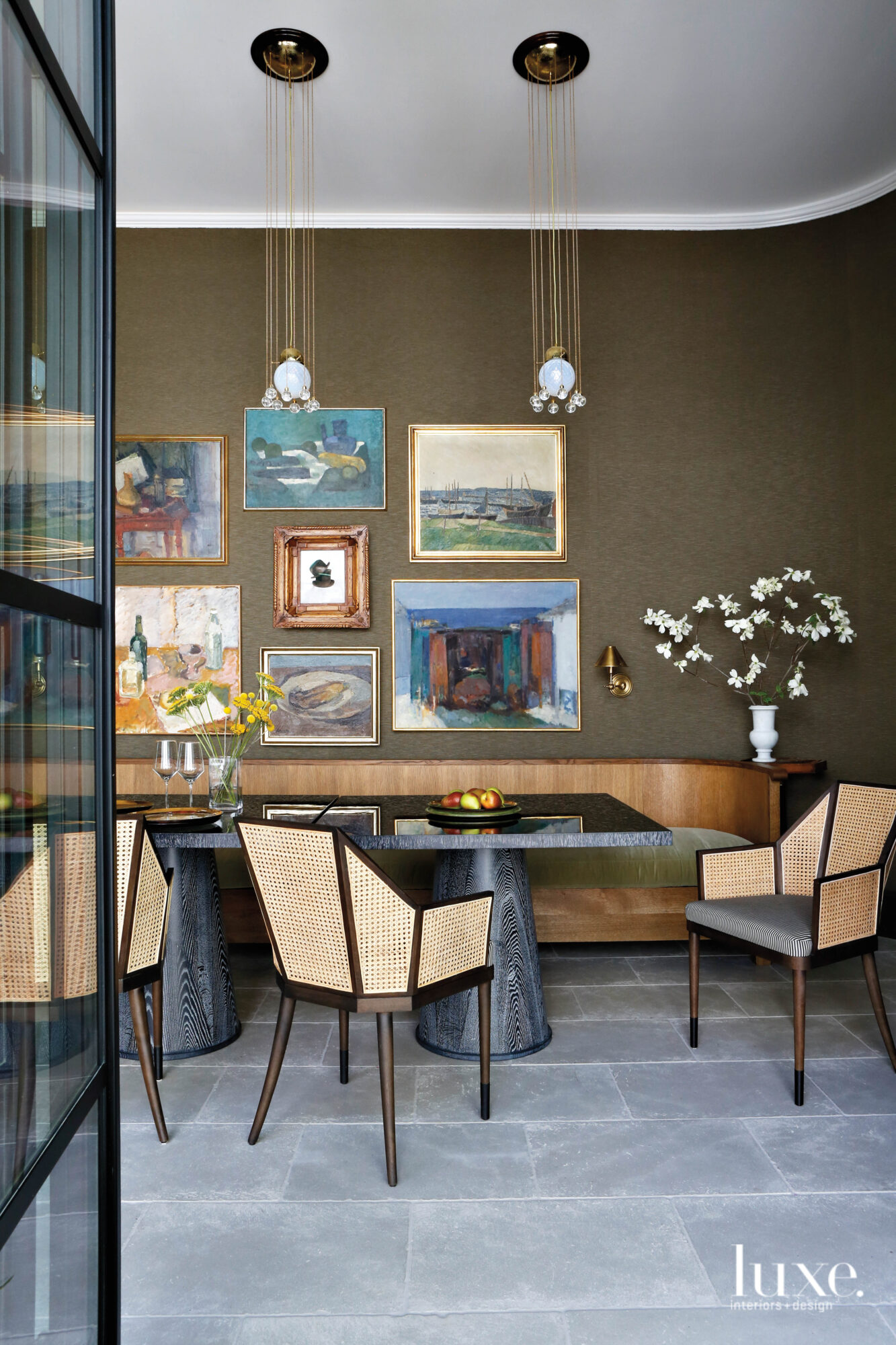 A dining room with a curved banquette, dark silk wall covering, modern armchairs and mismatched collage of framed wall art