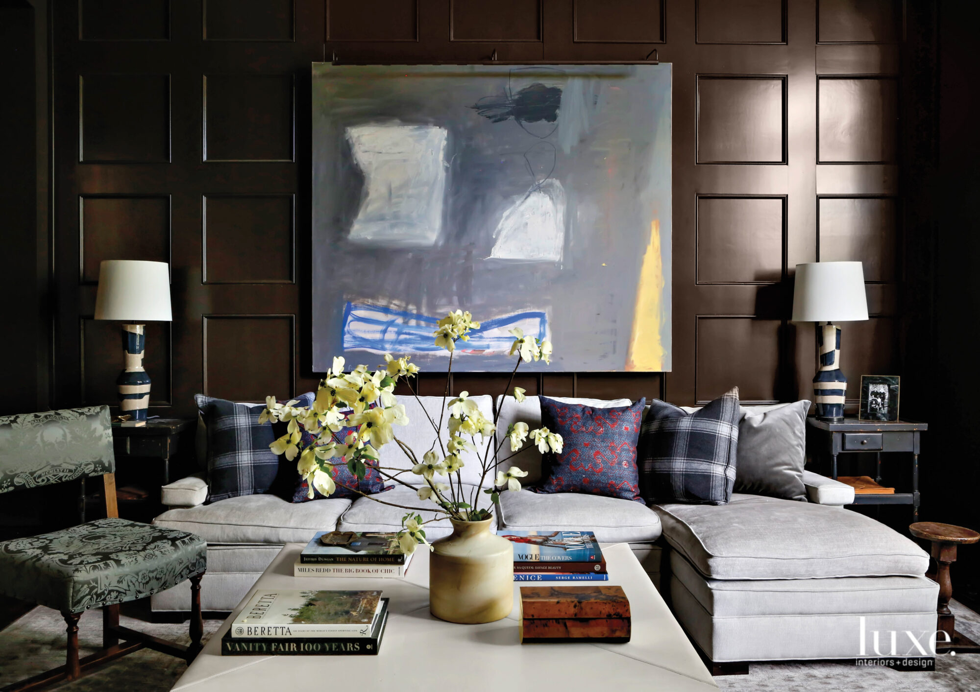 A family room paneled in dark, polished wood with an L-shaped sofa and large abstract artwork