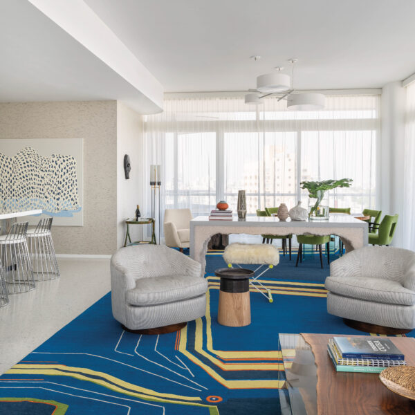 A Miami Beach Condo Balances Bold Interiors With Warm Tones Great room with blue and yellow rug, gray armchairs and a rock salt console table