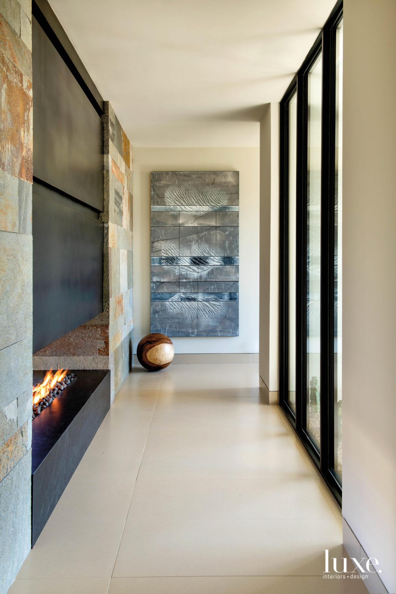 The hallway with a fireplace on the left and an abstract gray painting by Michael Kessler.