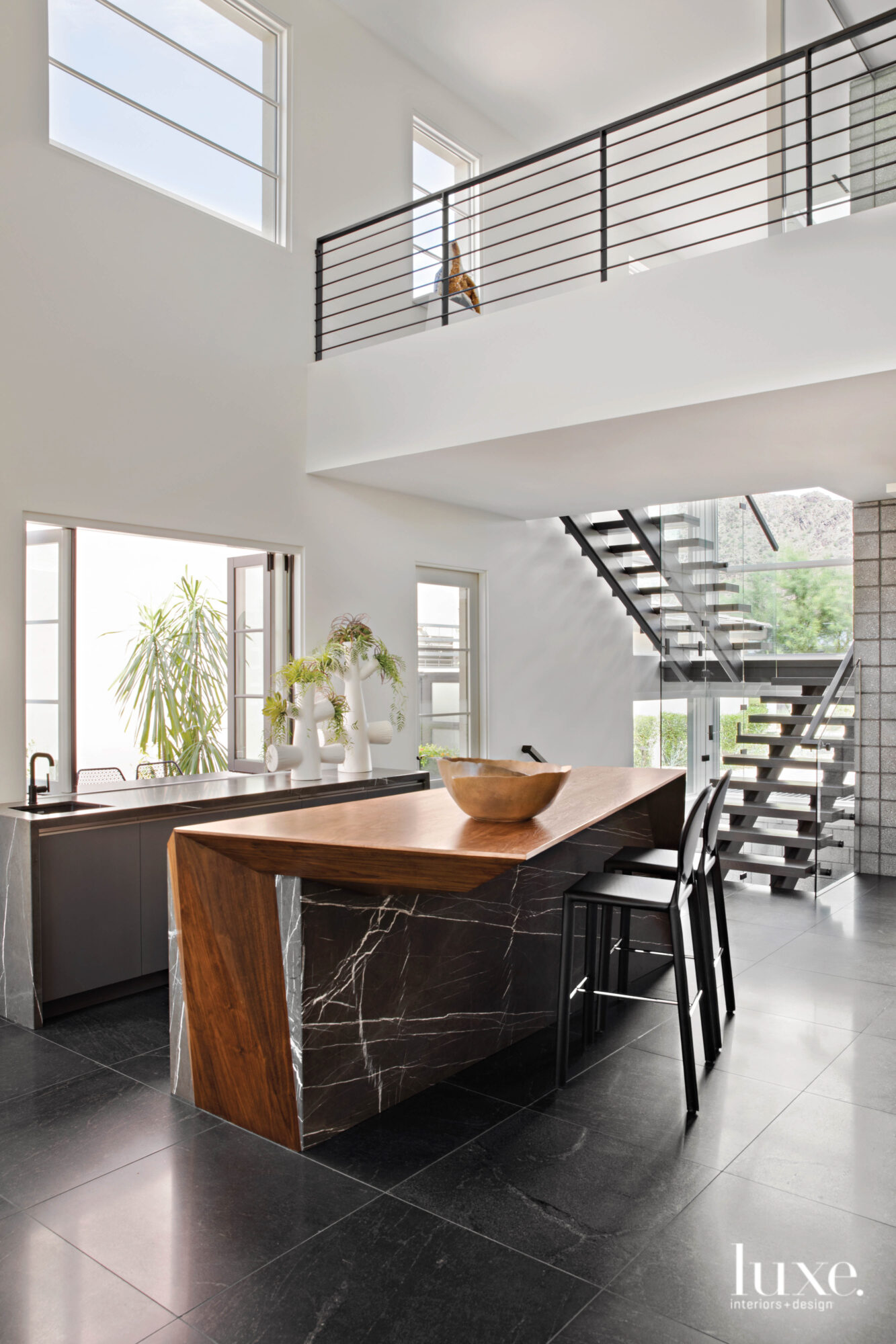 A wood-and-black-marble island in the kitchen with a floating staircase in the background.