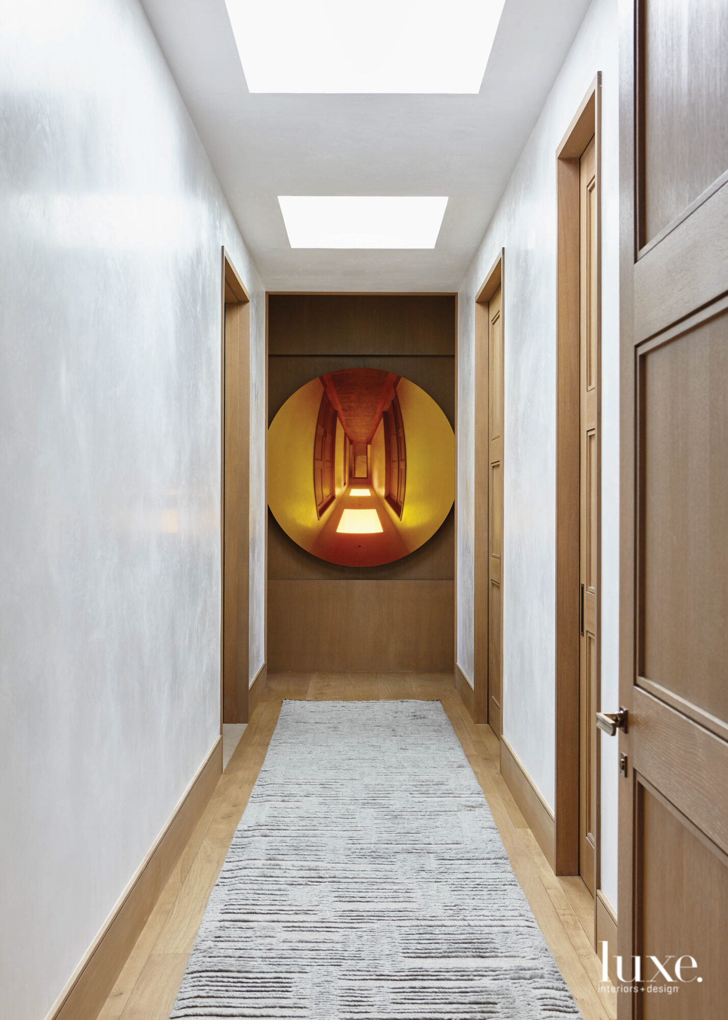 A hallway ends with a wall hung with a bronze mirror.