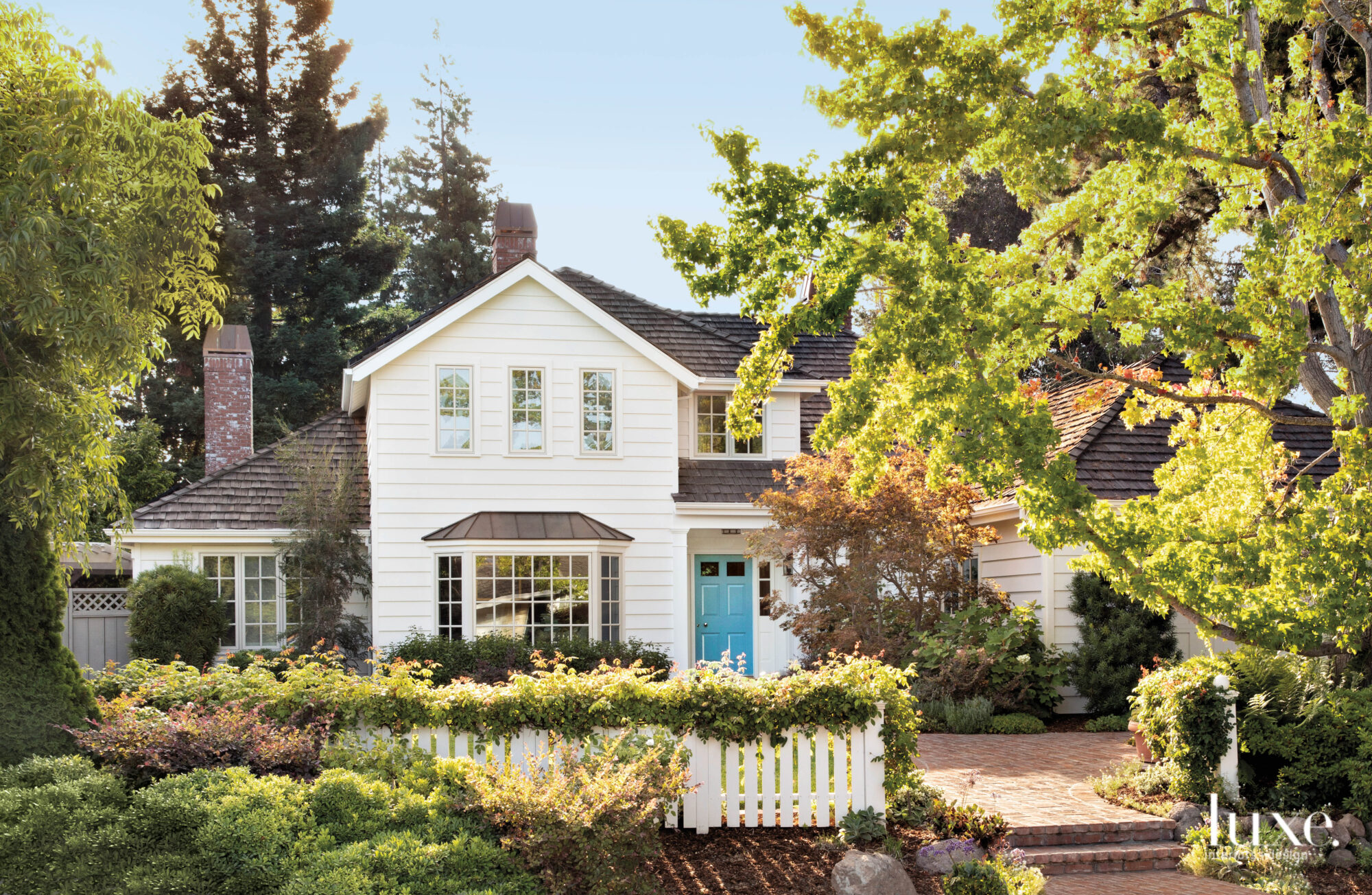 The exterior of the home is white with a blue door. It's surrounded by a lush, green garden.