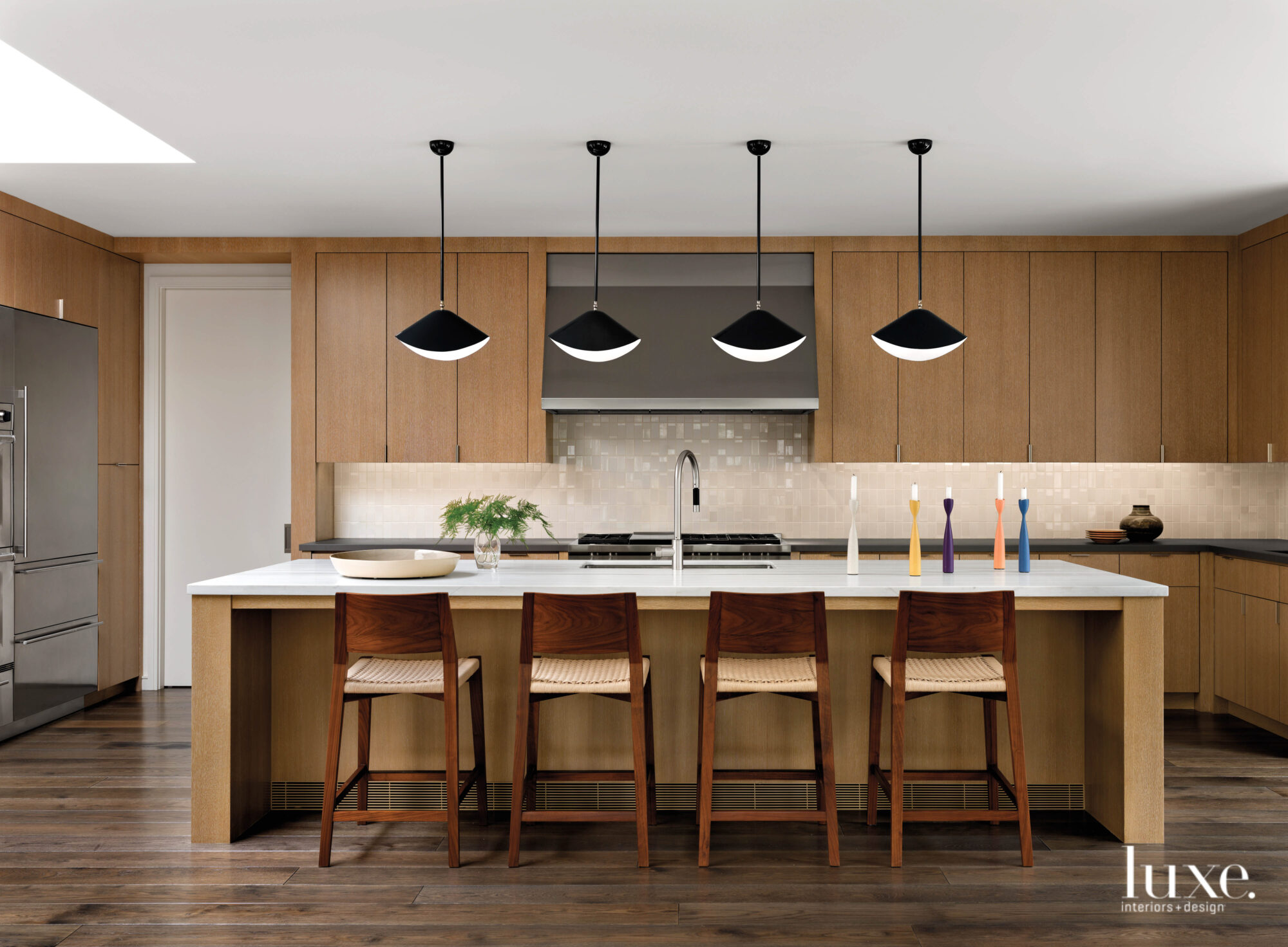 The kitchen has a large island lined by a row of seats and topped by a line of light fixtures.