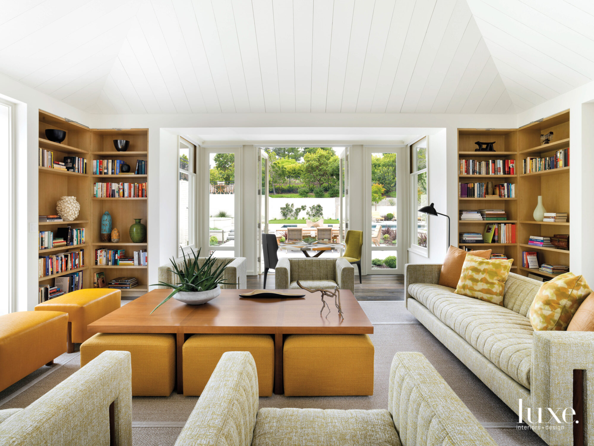 The family room's central piece is a large coffee table that has yellow stools underneath.