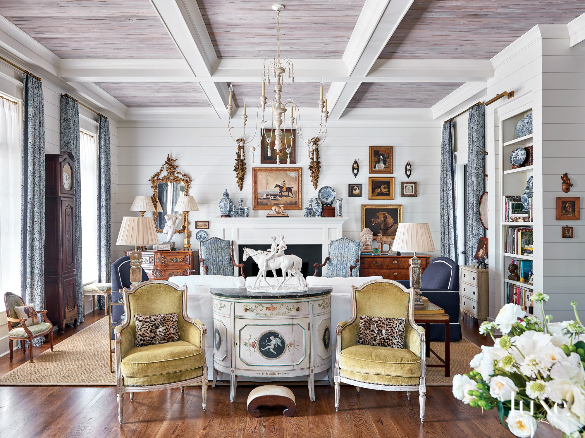 Living room with white walls, coffered ceilings, French armchairs, framed oil paintings and antiques