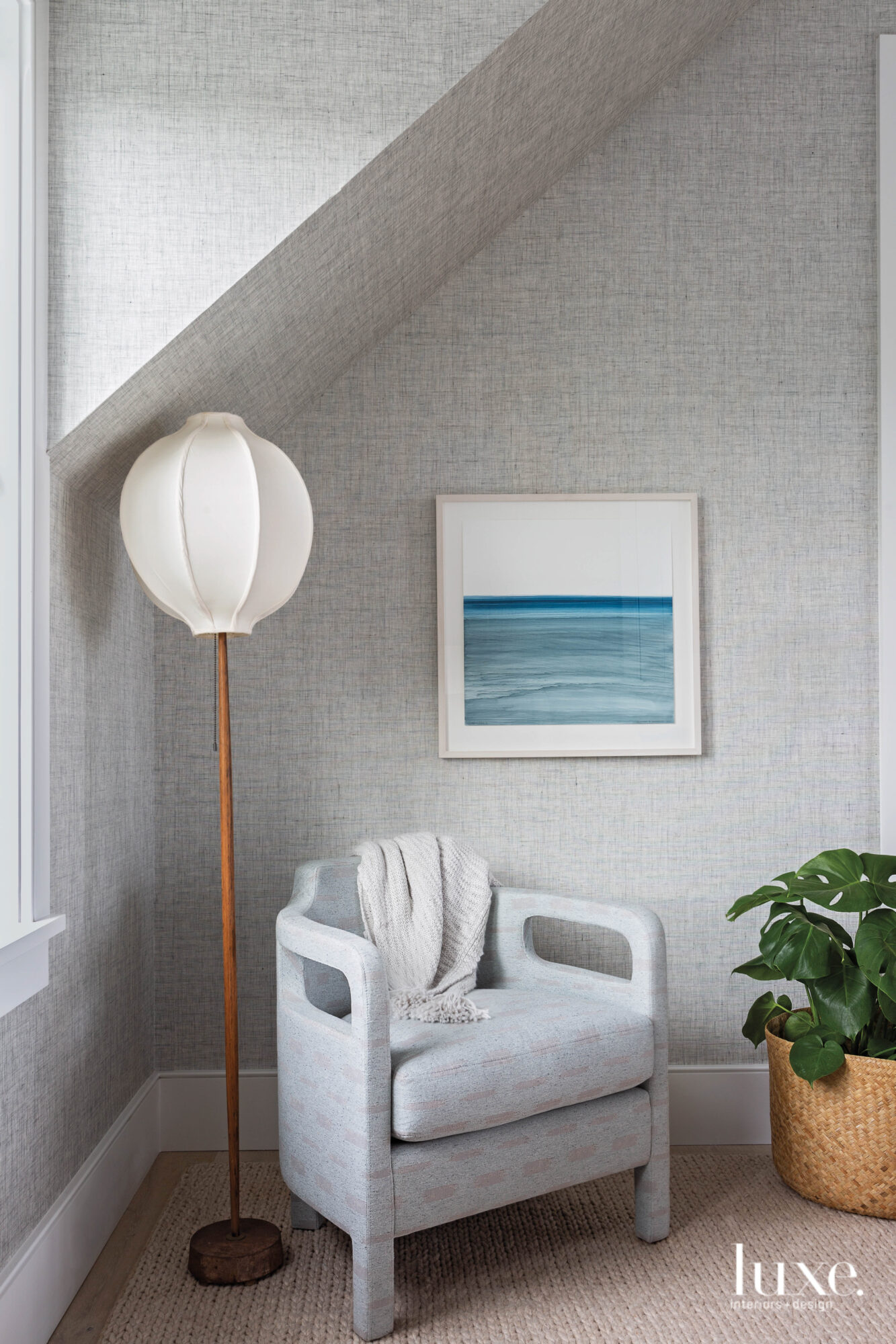 Corner of bedroom with crosshatched gray walls, comfortable armchair, floor lamp and ocean photography