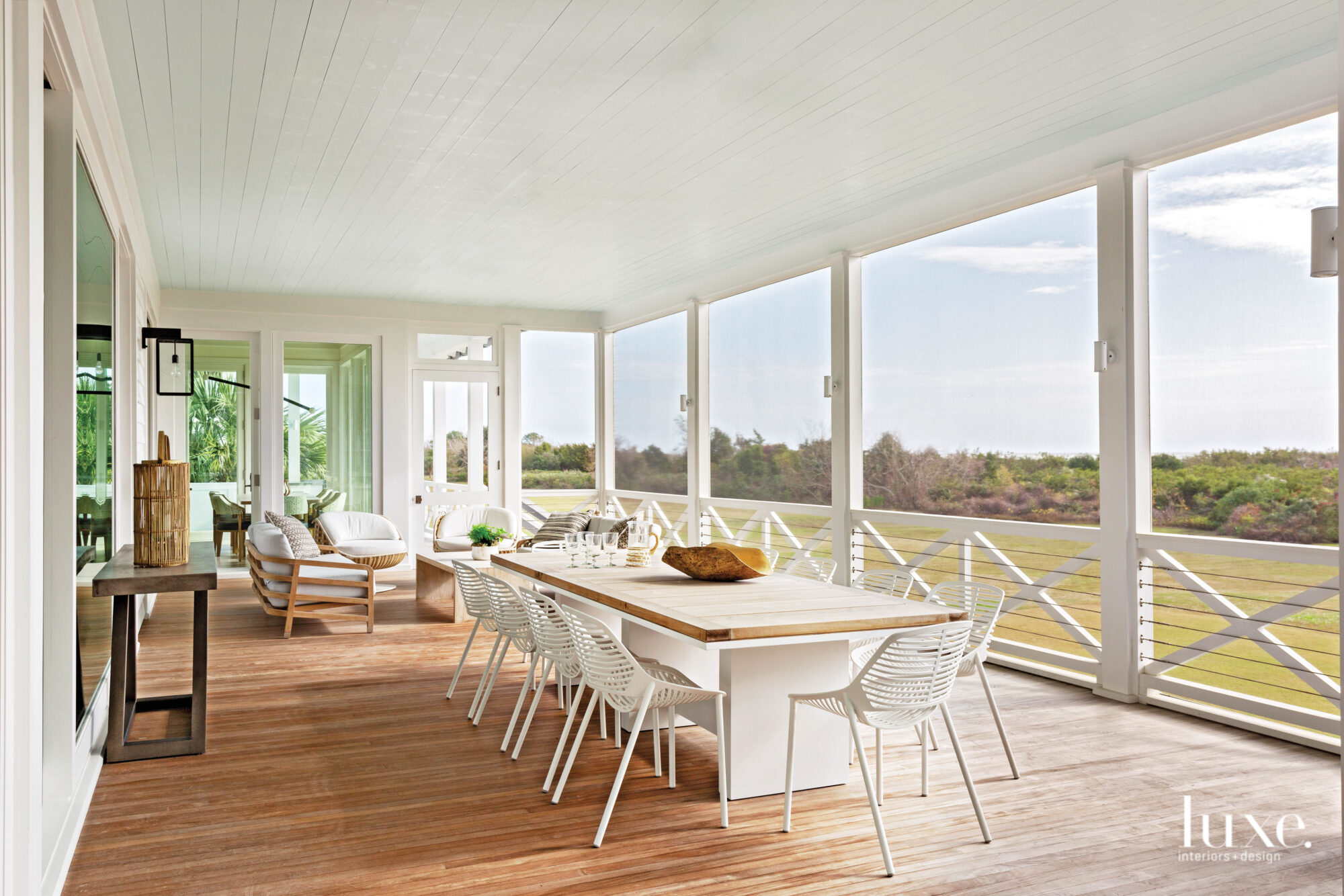 Screen porch with honey-colored wood floors, modern white dining table, modern white chairs, Lowcountry landscape