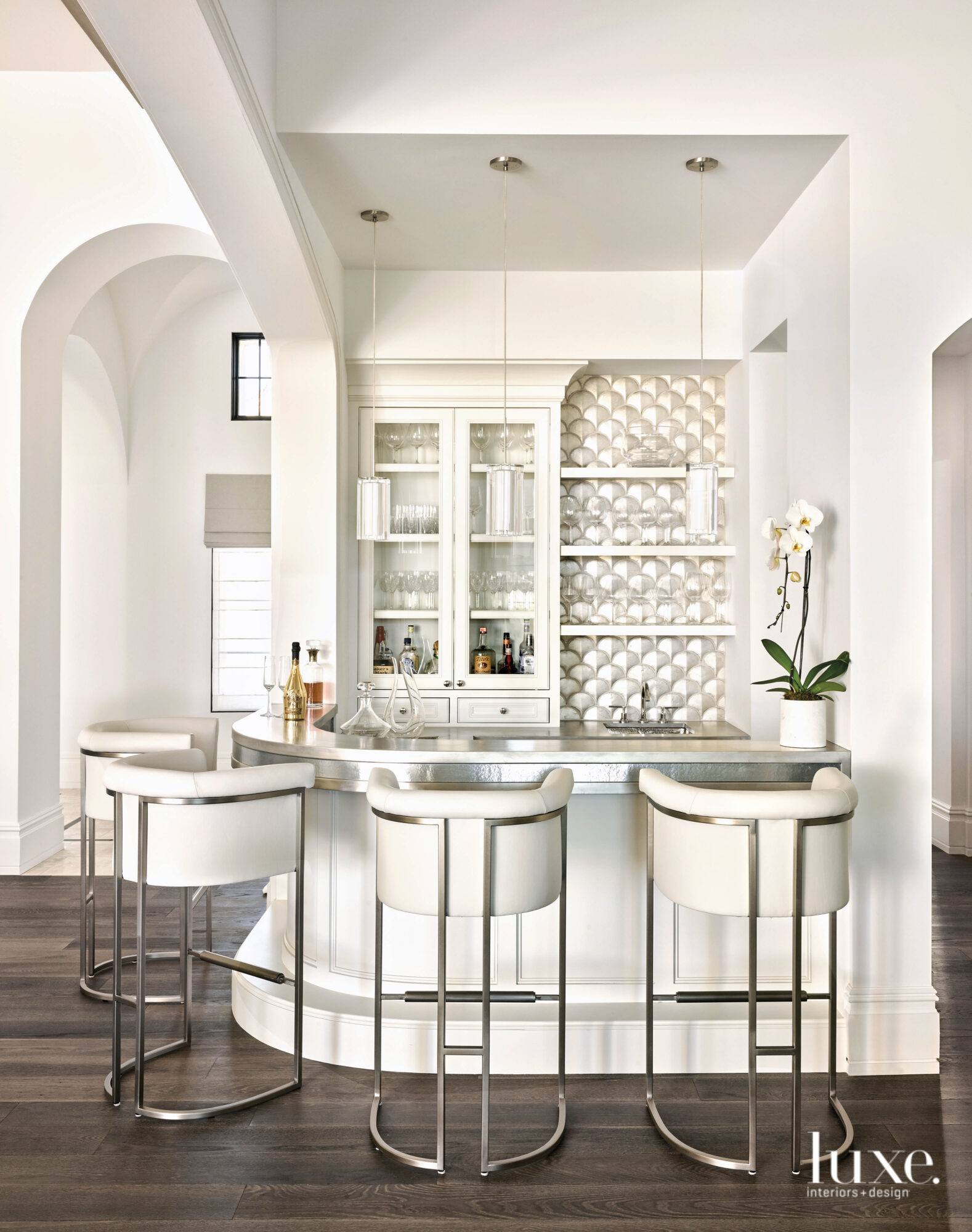 The all-white bar area has custom millwork and upholstered stools.